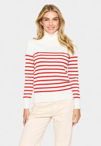 Red and white striped turtleneck sweater with a ribbed texture, featuring long sleeves and a fitted silhouette. Worn with beige pants.