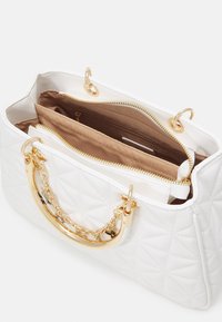Biała pikowana torba na ramię z uchwytem ozdobionym złotym łańcuchem, wnętrzem w brązowym materiale, z zapinanymi na zamek przegródkami i złotymi elementami metalowymi.