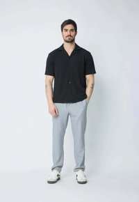 Chemise noire à manches courtes avec une texture subtile, fermeture à boutons ; pantalon gris clair à coupe ajustée, associé à des baskets blanches.