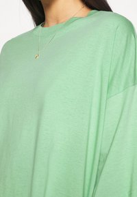 Camiseta verde de gran tamaño, hecha de un algodón suave y ligero. Presenta un cuello redondo sencillo y un ajuste holgado.