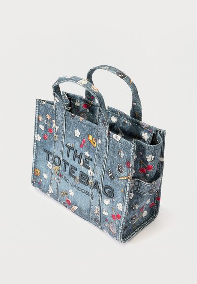 Denim tas met twee handvatten, versierd met kleine kleurrijke patches en de tekst "THE TOTE BAG MARC JACOBS" aan de voorkant.