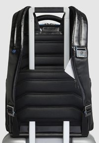 Zaino nero in nylon con sezioni imbottite e un elegante accento in pelle, dotato di spallacci regolabili e manico per aggancio al trolley.