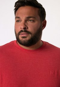Rotes Baumwoll-T-Shirt mit rundem Kragen und kurzen Ärmeln; hat ein dezentes, tonal gehaltenes Logo auf der linken Brust. Glatte Textur.