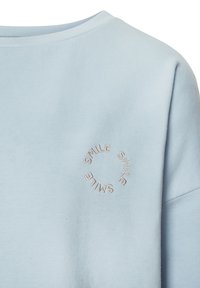 Sudadera azul claro con escote redondo, que presenta un bordado circular de "SMILE" en un color contrastante en la parte frontal. Textura suave.