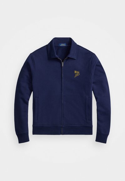 Ναυτικό μπλε φούτερ με φερμουάρ κατασκευασμένο από μαλακό ύφασμα, διαθέτοντας γιακά, δύο πλάγιες τσέπες και ένα χρυσό κεντητό λογότυπο στο άνω αριστερό μέρος του στήθους.