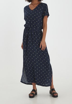 Granatowa sukienka w groszki z krótkimi rękawami, dekoltem w serek, paskiem w talii i bocznymi rozcięciami. Wykonana z lekkiej tkaniny, zdobiona żółtymi kropkami.
