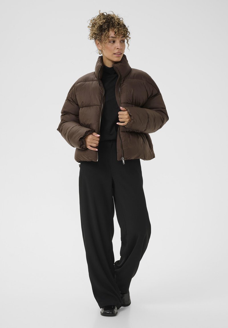 Rudas pūkuotas striukė su aukšta apykakle, siuvinėtu paviršiumi ir užtrauktuku. Derinama su juodomis plačiomis kelnėmis ir juodais bateliais.