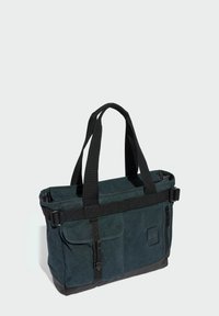 Dark green fabric bag with black accents, featuring dual handles, adjustable straps, flap pocket, and zipper closure. Textured, structured design.