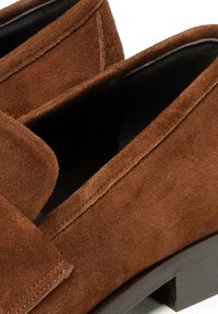 Mocassini in suede marrone con punta arrotondata e interno nero liscio. Le scarpe presentano un tacco basso e spesso e dettagli di cucitura lungo i bordi.