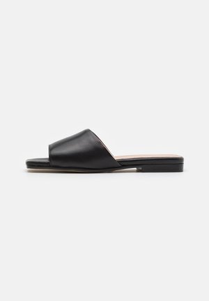 Sort læder open-toe slide sandal med flad hæl og bred rem over fronten, vist fra siden på hvid baggrund.