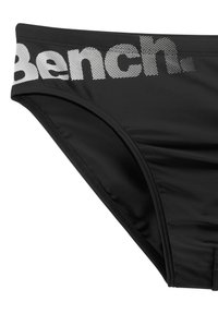 Crne bikinijeve gaće s širokim pojasom na kojem je otisnut "Bench." u bijeloj boji. Tkanina je glatka i rastezljiva s minimalnim šavovima.