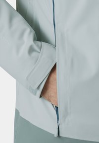 Lichtblauwe softshell jas met een ritszak, elastische manchetten en een gestroomlijnd ontwerp met een zachte textuur voor comfort.