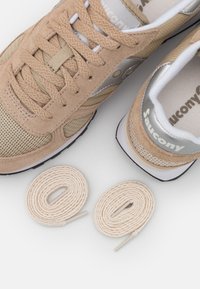 Béžové sportovní boty vyrobené z semiše a síťoviny, s kulatou špičkou, texturovanými tkaničkami a stříbrným logem. Součástí jsou dvě odpovídající tkaničky.