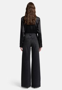 Czarna satynowa koszula z długim rękawem w połączeniu z ciemnymi, szerokimi jeansami z wysokim stanem. Kołnierz z wycięciami, zapięcia na guziki oraz dwie tylne kieszenie.