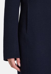 Marineblå uldfrakke med flad krave, lange ærmer og en sidelomme. Blød tekstur og skræddersyet design.