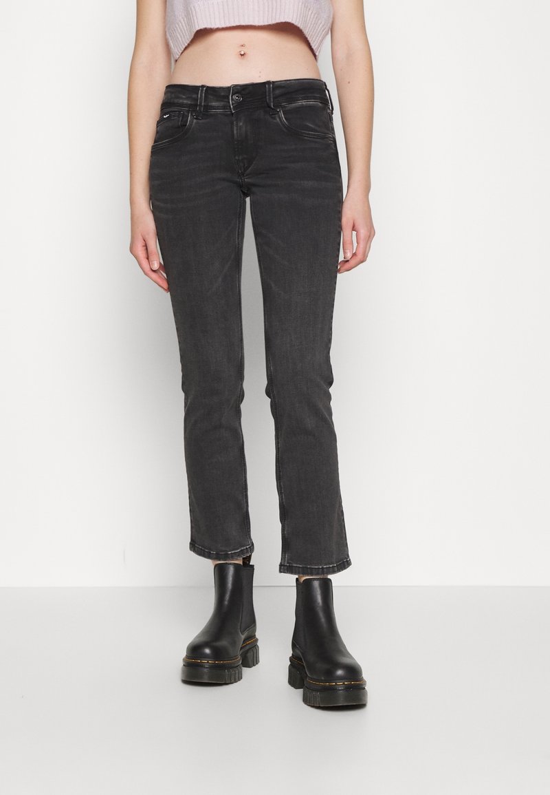 Svarta denimjeans med slim fit, kort längd, fem fickor och knappstängning. I kombination med svarta ankelboots.