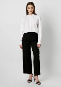 Weißes Hemd mit langen Ärmeln, kombiniert mit hoch taillierten schwarzen weit geschnittenen Hosen und schwarzen Riemchen-Heels. Einfaches und modernes Design.