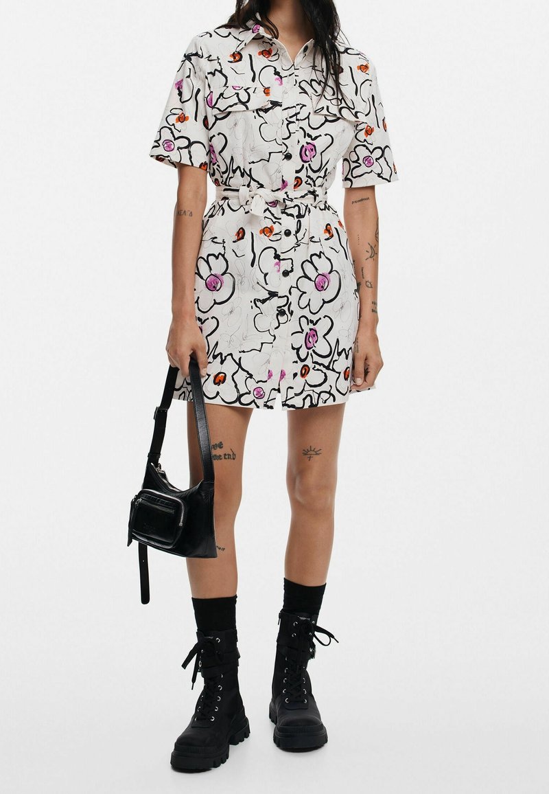 Robe à manches courtes avec ceinture, blanche, ornée de motifs floraux colorés et de lignes. Associée à un sac à main noir et des bottes de combat noires à lacets.
