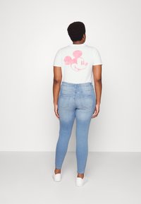 Tricou alb cu un grafic roz cu Mickey Mouse, asortat cu blugi skinny albaștri. Modelul poartă adidași albi, evidențiind o ținută casual.