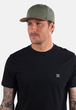 Casquette vert olive avec une visière plate, ornée d'un logo brodé. T-shirt noir à manches courtes avec un petit graphique blanc sur la poitrine.