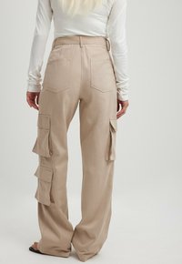Beige cargo kalhoty s volným střihem, které mají boční kapsy, dvě zadní kapsy a texturovanou tkaninu s hladkým povrchem.