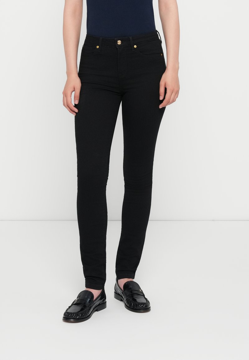 Jeans skinny neri in denim con vita alta, due tasche frontali e dettagli in metallo dorato. Abbinati a mocassini neri.