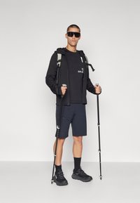 Utendørsutstyr: svart jakke med glidelås, svart skjorte med logo, marineblå shorts, svarte tursko, turstenger, solbriller; minimalistisk design.