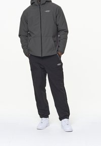 Grå zip-up huvtröja med elastiska ärmar, kombinerad med svarta cargobyxor. Båda har logotypdetaljer. Vita sneakers kompletterar outfiten.