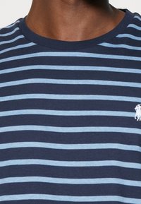Navy blue striped t-shirt with light blue horizontal stripes. Crew neckline and small white logo detail on the chest. Soft cotton fabric.