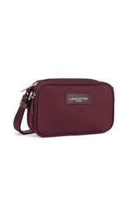Piccola borsa crossbody rettangolare color marrone bordeaux con doppie tasche a zip e logo "Lancaster Paris" sul pannello frontale.