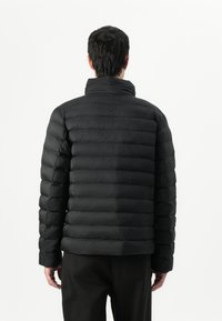 Zwarte pufferjas met horizontale quiltstructuur, hoge kraag en elastische manchetten. Glad, glanzend weefsel met een lichtgewicht, gewatteerd ontwerp.