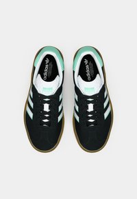 Zapatillas Adidas negras con rayas blancas, detalles en verde menta, lengüeta blanca texturizada y suela de goma vistas desde arriba sobre un fondo blanco.