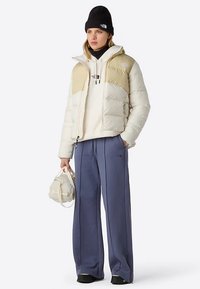 Witte en beige puffy jas, licht sweatshirt, losse blauwe broek en een zwarte muts. Accessoires zijn onder andere een kleine witte tas.