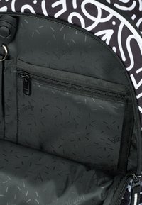 Interno di uno zaino nero con motivi bianchi, dotato di una tasca con zip e fodera in nero testurizzato con dettagli stampati discreti.