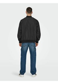Black bomber jacket with ribbed cuffs and hem, paired with light-wash cargo jeans featuring multiple pockets and a relaxed fit.