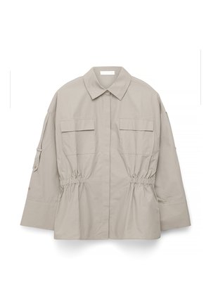 Bež dolgo rokavna jakna s koničastim ovratnikom, dvema sprednjima žepoma s poklopcem, nabranim pasom in detajlom z gumbi na rokavih, položena na belo podlago.