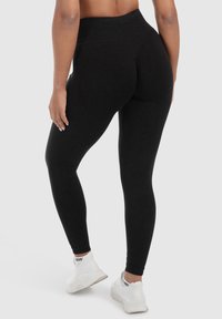 Leggings neri a vita alta realizzati in tessuto elastico con una texture liscia, caratterizzati da un design aderente e lunghezza alla caviglia, abbinati a sneakers bianche.