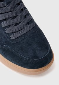 Baskets en daim bleu marine avec des lacets épais bleu marine et une semelle en caoutchouc brun clair sur un fond blanc.
