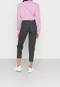 Grå högmidjade jeans med rakt ben, med bakfickor och denimtextur, kombinerat med en pastelllila sweatshirt och vita sneakers.