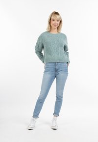 Világoskék kötött pulóver, textúrált mintával, világoskék farmernadrággal és fehér sportcipővel párosítva. Lazán álló, kényelmes fazon, bordás aljjal.