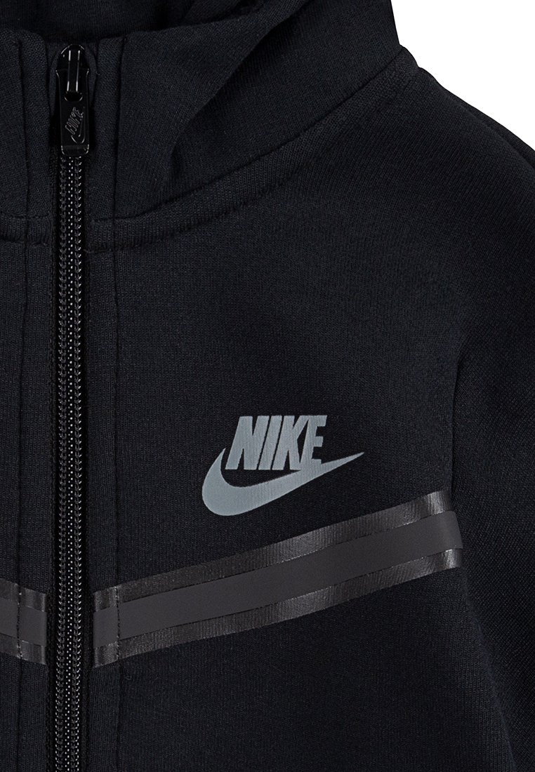 Hoodie zippé noir en tissu doux. Présente un logo Nike gris et des rayures noires horizontales sur la poitrine. Tirette de fermeture éclair texturée.