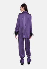 Purple satin pajama set featuring decorative patterns, feather accents on sleeves, and drawstring cuffs on pants.