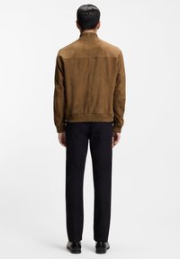 Brun mockajacka med ribbad krage och muddar, med en slät, matt textur, kombinerad med svarta byxor och skor.