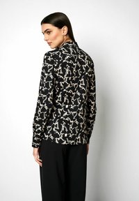 Langärmlige Bluse aus schwarzem Stoff mit einem cremefarbenen abstrakten Blumenmuster. Mit klassischem Kragen und Knopfschluss hinten.