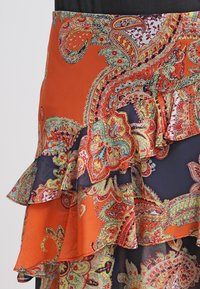 Oranssi ja laivastonsininen hame paisley-kuviolla ja röyhelöyksityiskohdilla. Valmistettu kevyestä kankaasta, jonka koristeina monimutkaiset kuviot ja kontrastivärejä.