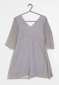 Robe à motif floral bleu clair avec des éléments orange et verts, dotée d'un décolleté en V, de manches trois-quarts et d'une jupe fluide. Accrochée à un crochet noir.