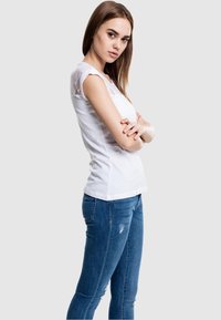 Camisa blanca de manga corta con detalles de encaje en los hombros, combinada con jeans ajustados azules con ligeras desgastes.