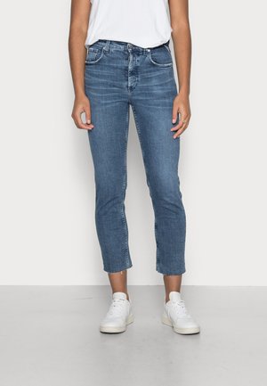 Ανοιχτό μπλε τζιν ψηλής μέσης με στενή γραμμή και κομμένο στρίφωμα. Διαθέτει πέντε τσέπες και απαλό ξεθώριασμα. Συνδυασμένο με λευκά αθλητικά παπούτσια.