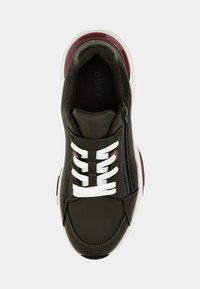 Ciemnozielone sneakersy z białymi sznurówkami i zamkiem błyskawicznym, wykonane z teksturowanej tkaniny z błyszczącymi bordowymi akcentami na podeszwie. Widoczne logo.