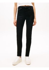 Slim-fit black jeans worn with white sneakers and a white cropped top, shown from waist to feet on a plain background.